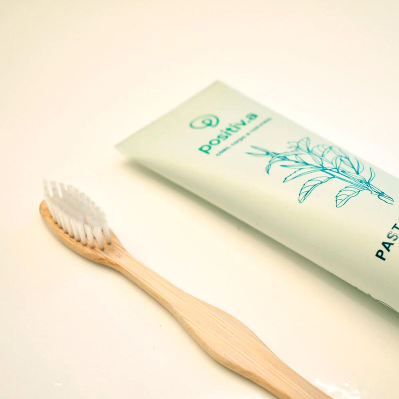 escova de dente de bambu da Positiv.a ao lado de uma pasta de dente da mesma marca